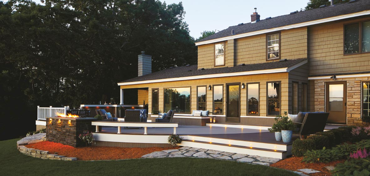 A low-profile deck connected to the house shows just a few steps to the deck with a built-in bench rail and beautiful outdoor furniture. 