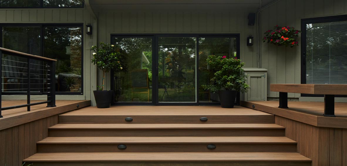 Wide steps lead to a deck that extends on either side of the stairs with a sliding glass door in the center view.