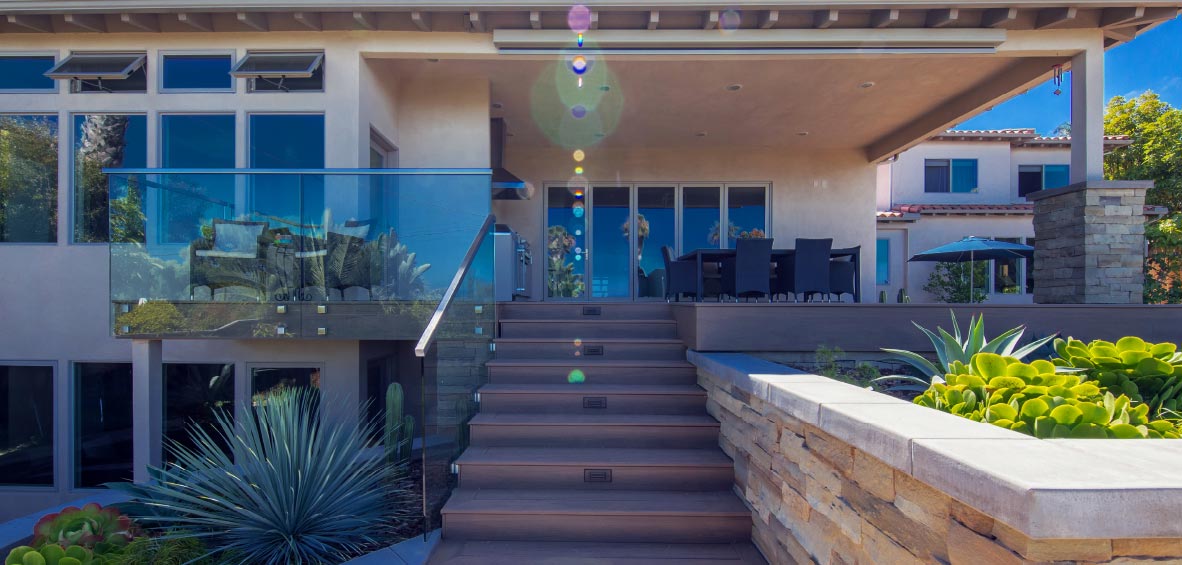 Stairs climb to a raised deck with landscaping below one side and a raised stone planter along the other.