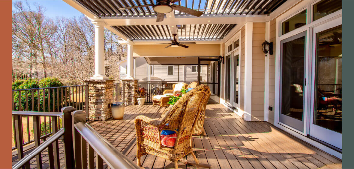  A sunny deck with woven furniture looks over the yard with a pergola and open louvers installed above.
