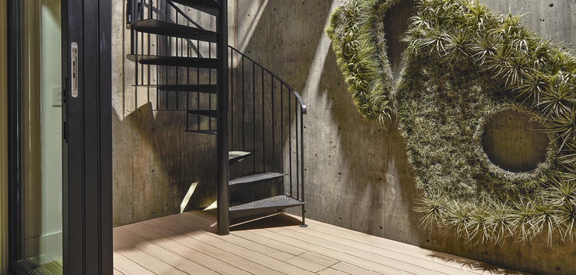 A black spiral staircase sits in the corner of a room and leads to a deck above.