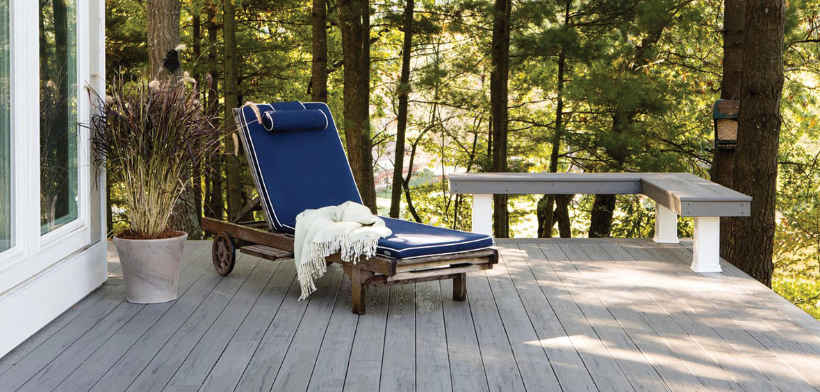 A small deck shows a lounge chair and potted plant next to a built-in bench along the corner perimeter.