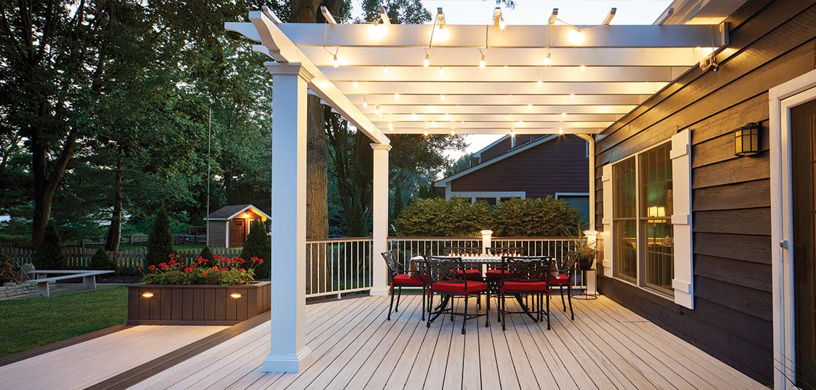 A back deck hosts a dining table with a pergola overhead, which illuminates the living area with string lights woven between louvers. 