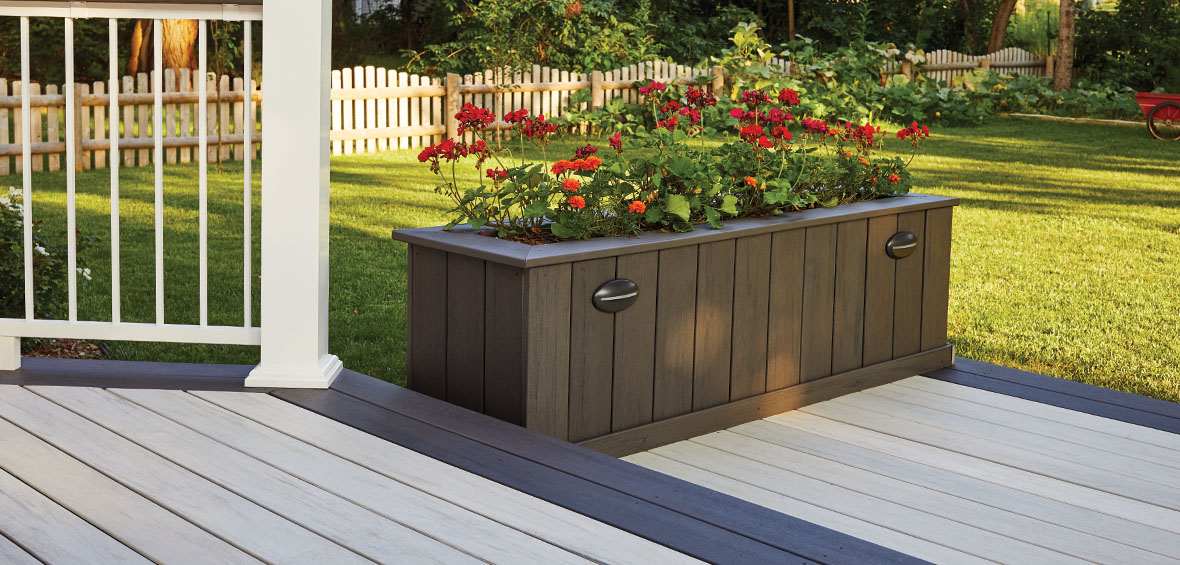A built-in planter box lines the edge of a small deck platform and has red flowers blooming from the top.
