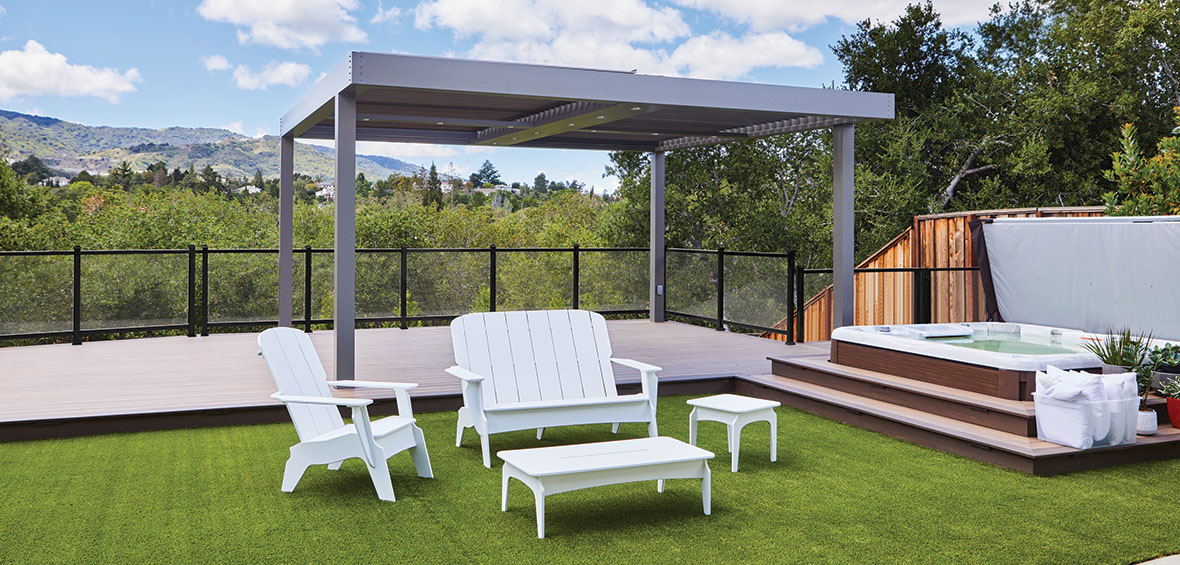 Outdoor seating sits on turf with a platform deck and pergola just a step up behind it, and a hot tub to the left.