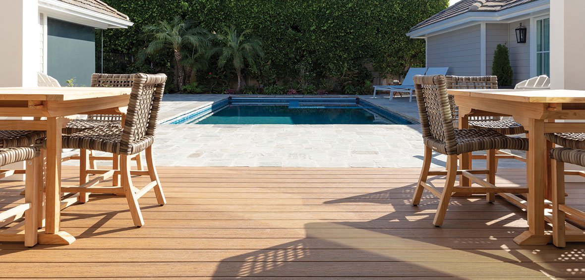 A low-lying deck with dining sets on each side seamlessly transitions to a patio featuring an in-ground pool.