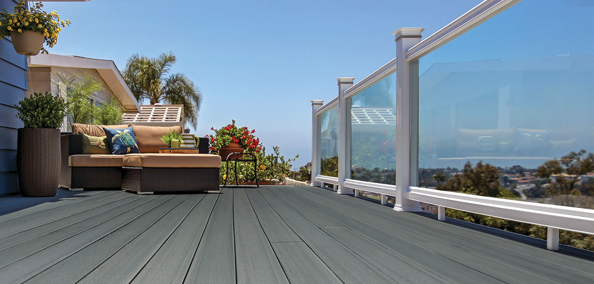An outdoor couch on a small gray deck faces glass railing that offers an unobstructed view of the neighborhood.