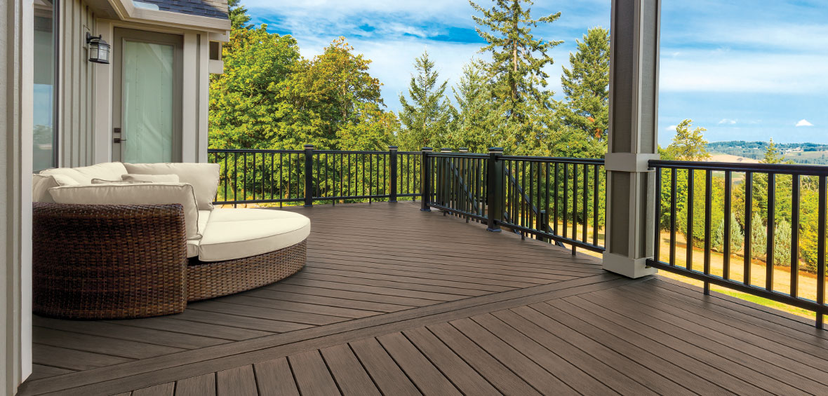 A dark brown deck with black railing and creative decking patterns has a single, round, woven loveseat for relaxation.