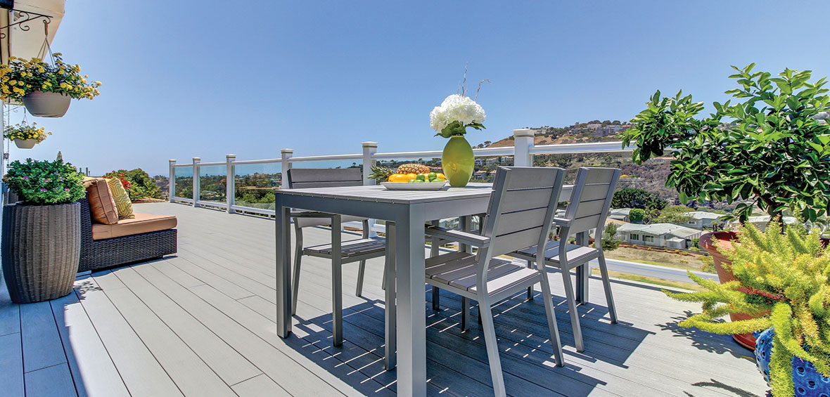 A dining table separate from a sitting area includes hanging plants and varied pot sizes for visual interest in the small deck’s design.