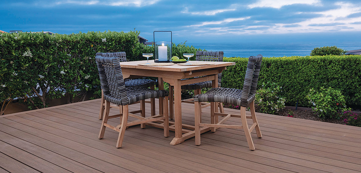 A low-lying deck with a dining table is surrounded by landscaping and tall hedges for privacy and beauty.