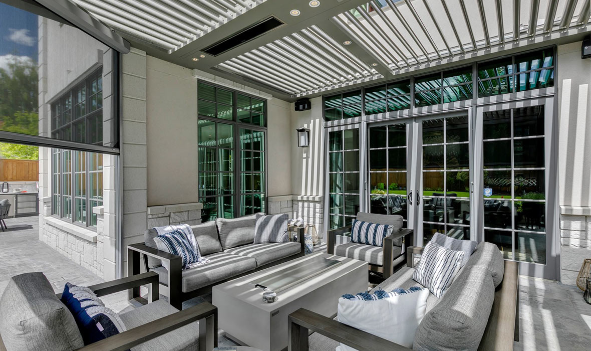 A deck includes outdoor couches, chairs, and a coffee table shaded by adjustable shades.