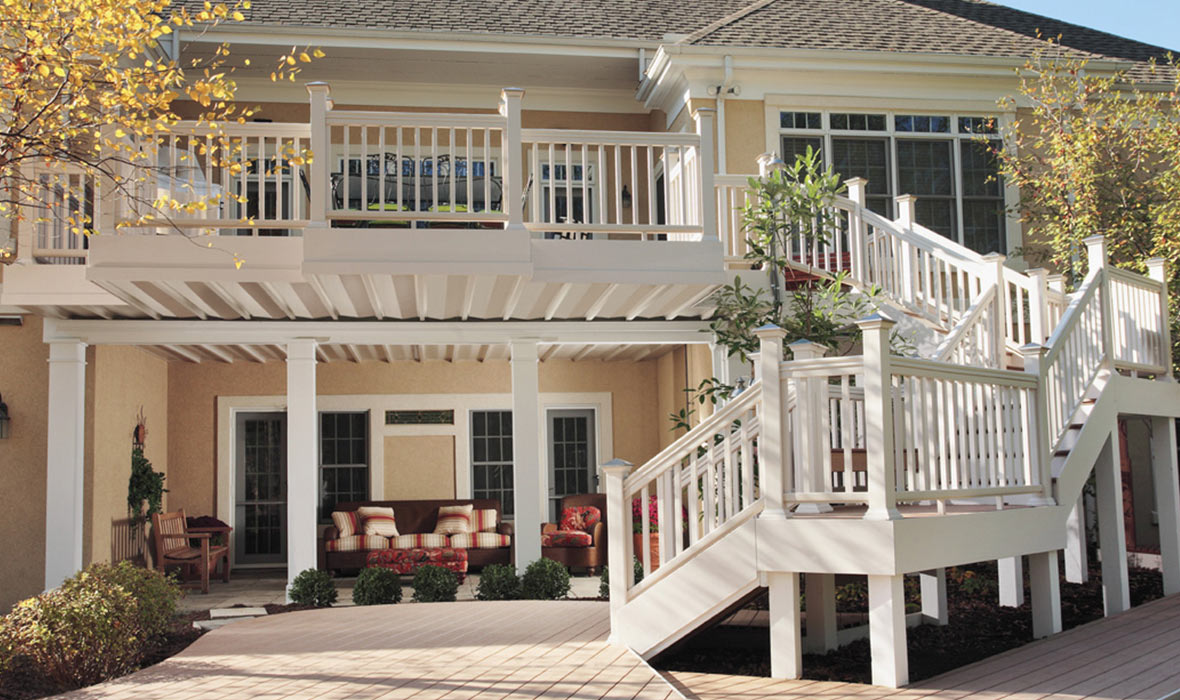 A shaded patio with outdoor furniture sits beneath a raised deck, keeping it shaded from the sun.