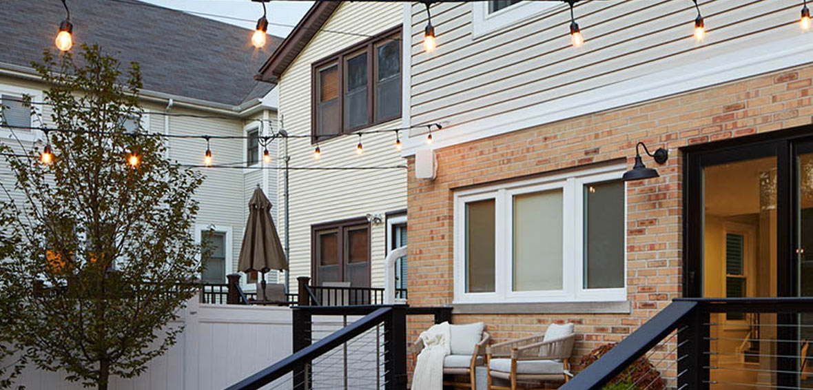 A backyard view of a townhouse with bistro lights above deck.