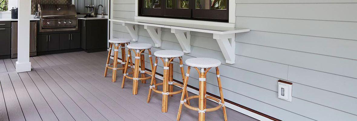 Four bamboo bar stools with white seats are placed in front of a bar counter on a deck kitchen space.