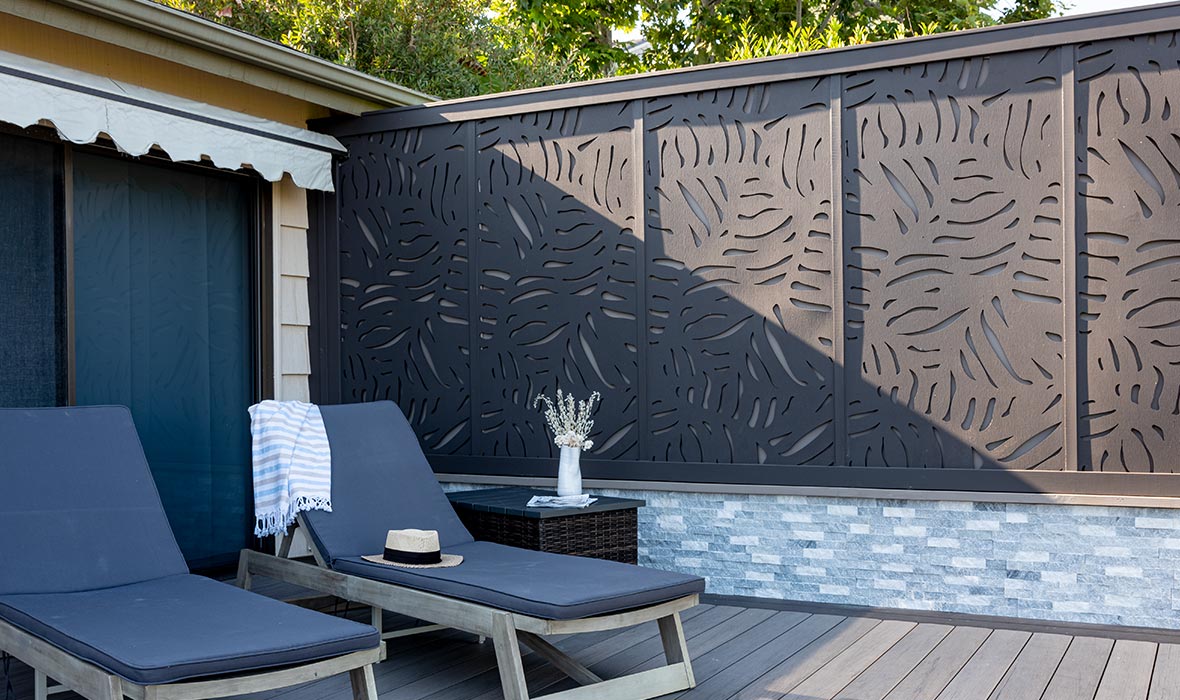 Two lounge chairs and an end table are shielded from the sun due to decorative fencing.