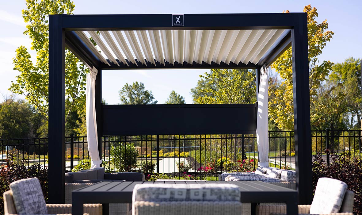 A cabana with curtains protects a casual seating area with two couches in a garden.