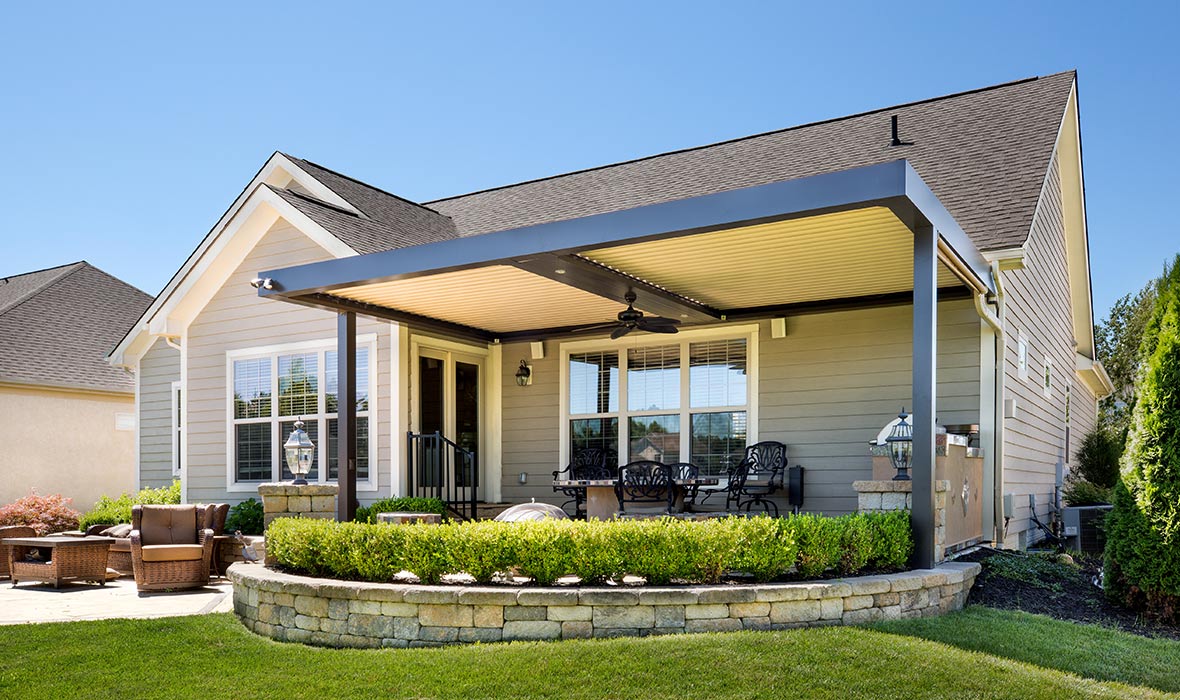 A pergola over a back patio includes motorized louvers and a ceiling fan. 