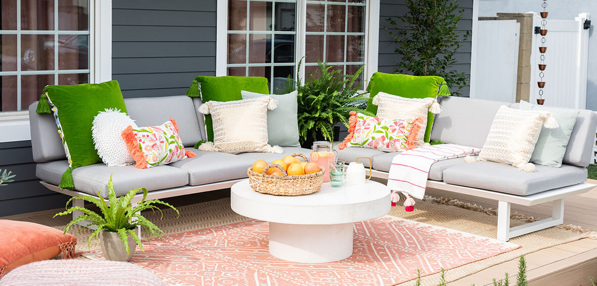 A small deck makes the most of its space with a peach rug, two outdoor sofas, a coffee table, and plenty of throw pillows.