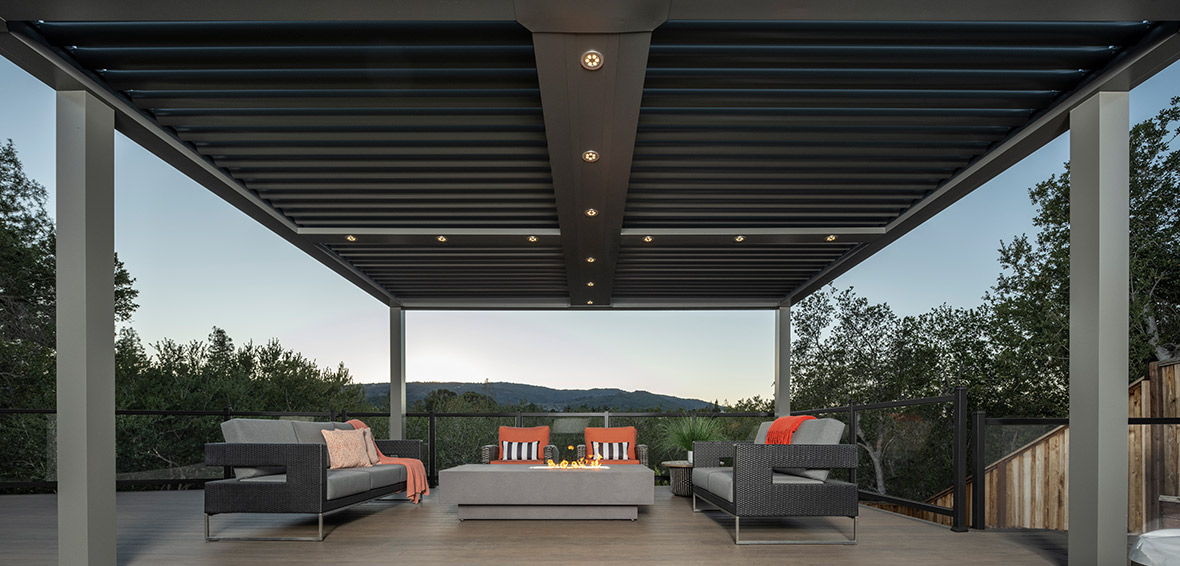 A pergola over a deck and furniture features recessed ceiling lights.