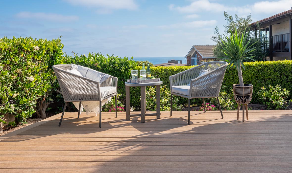 A seating arrangement on a deck is protected from the sun by potted shade trees.
