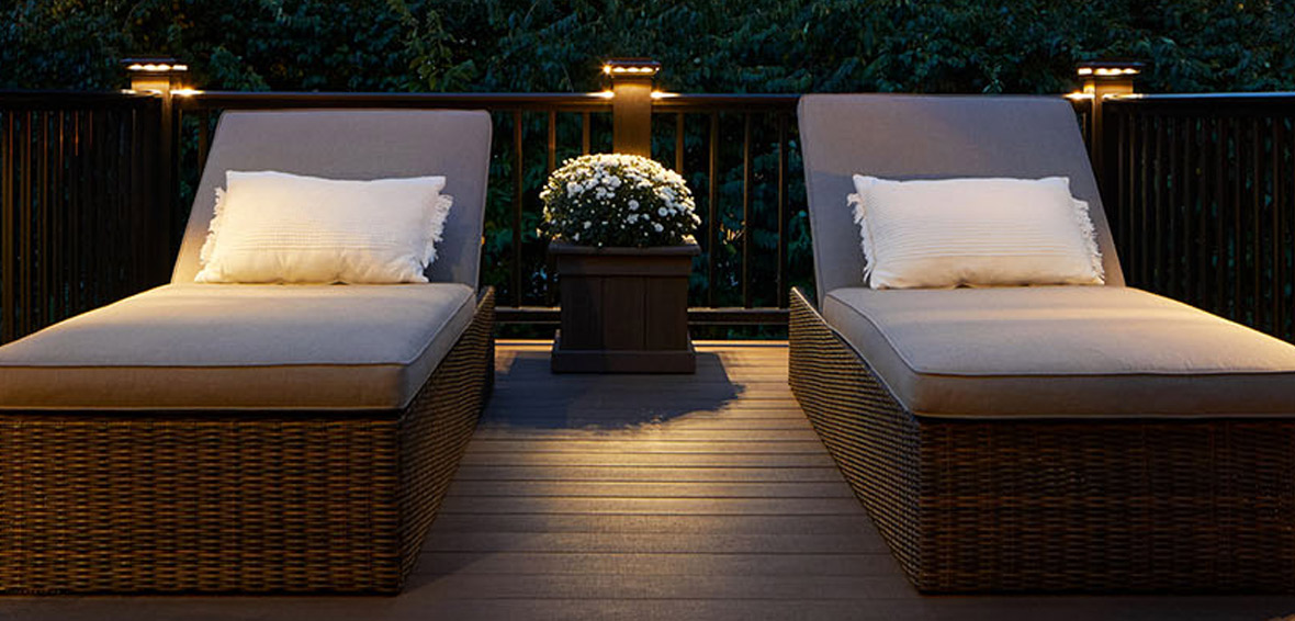 Two lounge chairs on an outdoor deck with post cap lights providing a gentle glow.