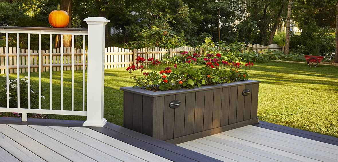 Red flowers bloom from the top of a custom raised planter installed on a lower deck level. 