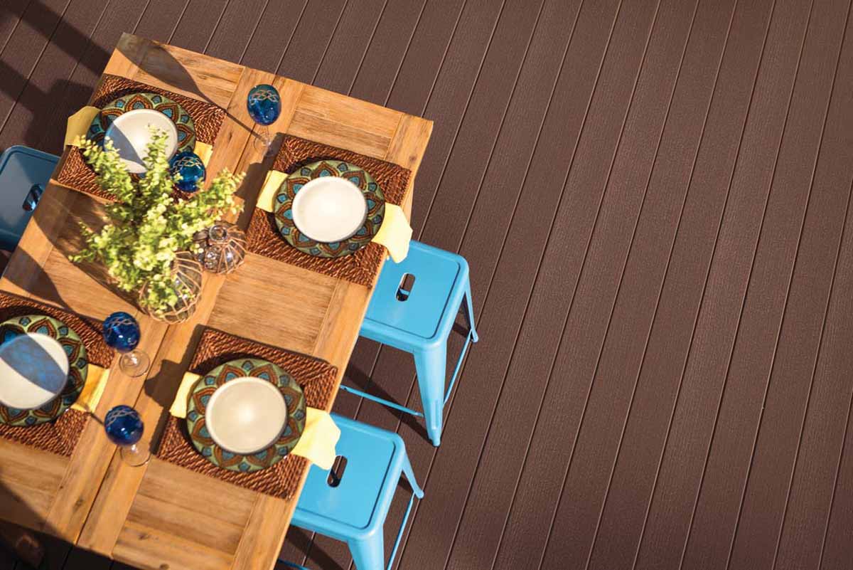 A farmhouse-style light brown wooden dining table is set on a richly hued dark brown deck