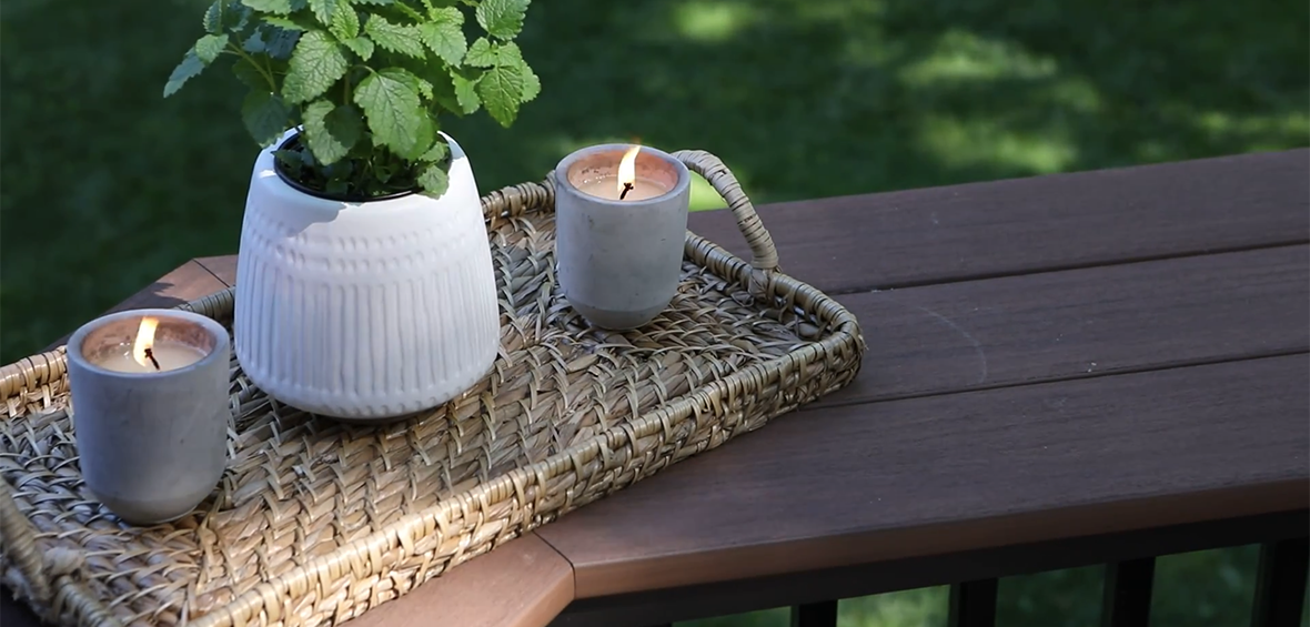 A close up of a top rail showcases the wide, flat-topped TimberTech Drink Rail with a potted herb and candles on top.