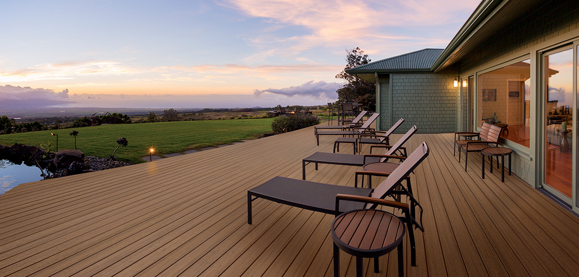 A composite deck at sunset looks out over a sprawling back garden and pond. 