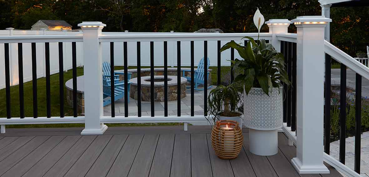 White railing with black balusters lines the perimeter of a deck and features lights built into the railing post caps. 