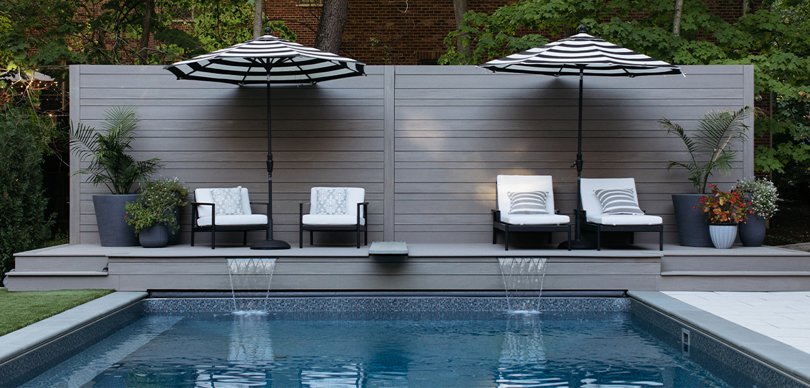 A poolside deck with umbrella-covered seating features waterfall spouts feeding into the pool. 