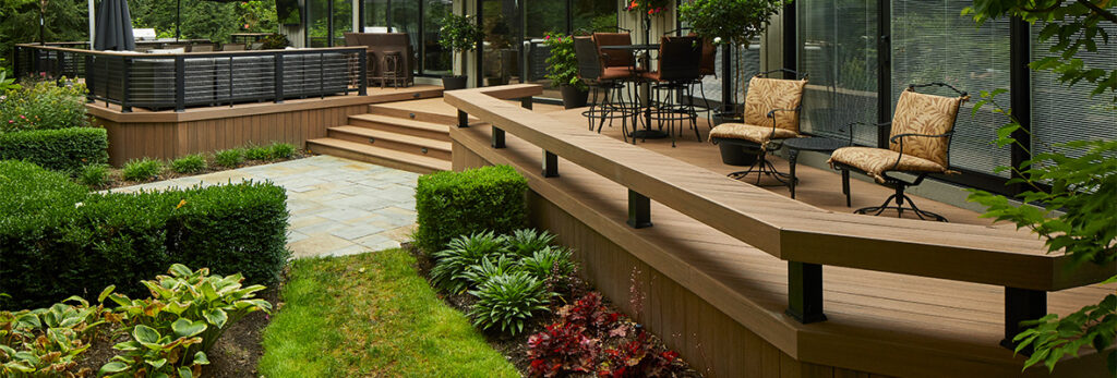 A large back deck features built-in bench railing, a stone pathway, and polished landscaping for a beautiful garden.