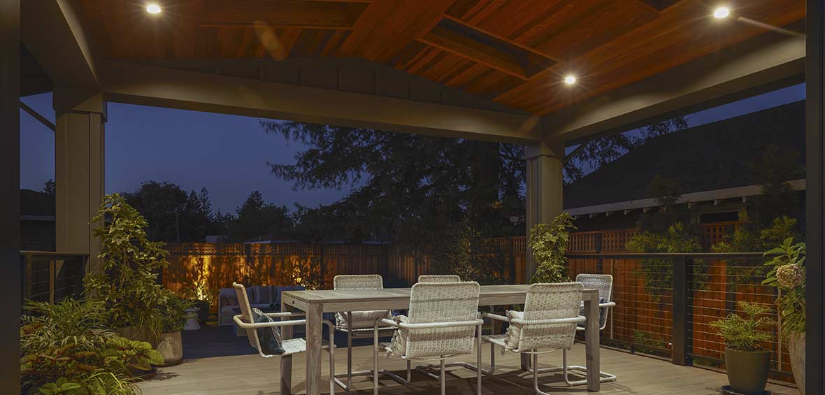 A back deck with a dining set is protected by an overhead cover with recessed lights built-in. 