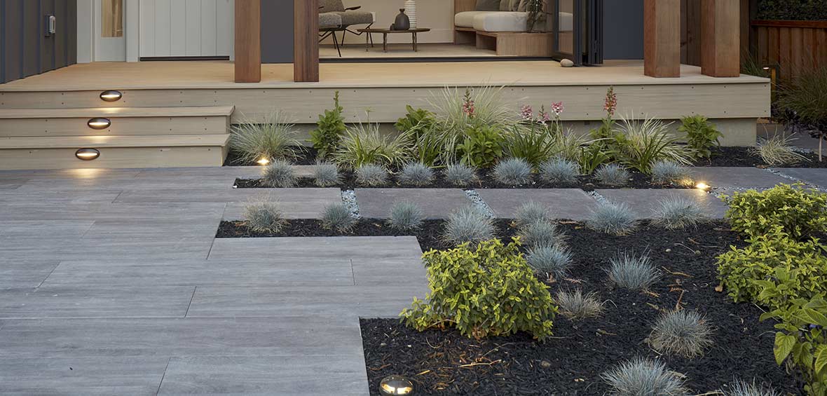 A path up to a front porch is surrounded by low-lying landscaping with ground-level landscaping lights throughout. 