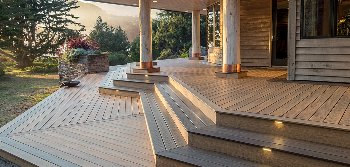 A wraparound deck features a water chain, built-in riser lights, and is covered in an evening sunset glow. 