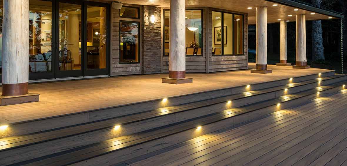 A multi-level deck features lights built into each stair riser leading up to a backdoor and bay window. 