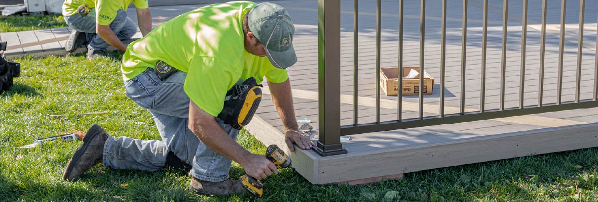 A contractor installs rim boards with a power driver to a newly installed deck.