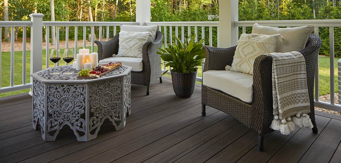 Two outdoor armchairs with upholstered cushions feature plump throw pillows and a tasseled blanket. 