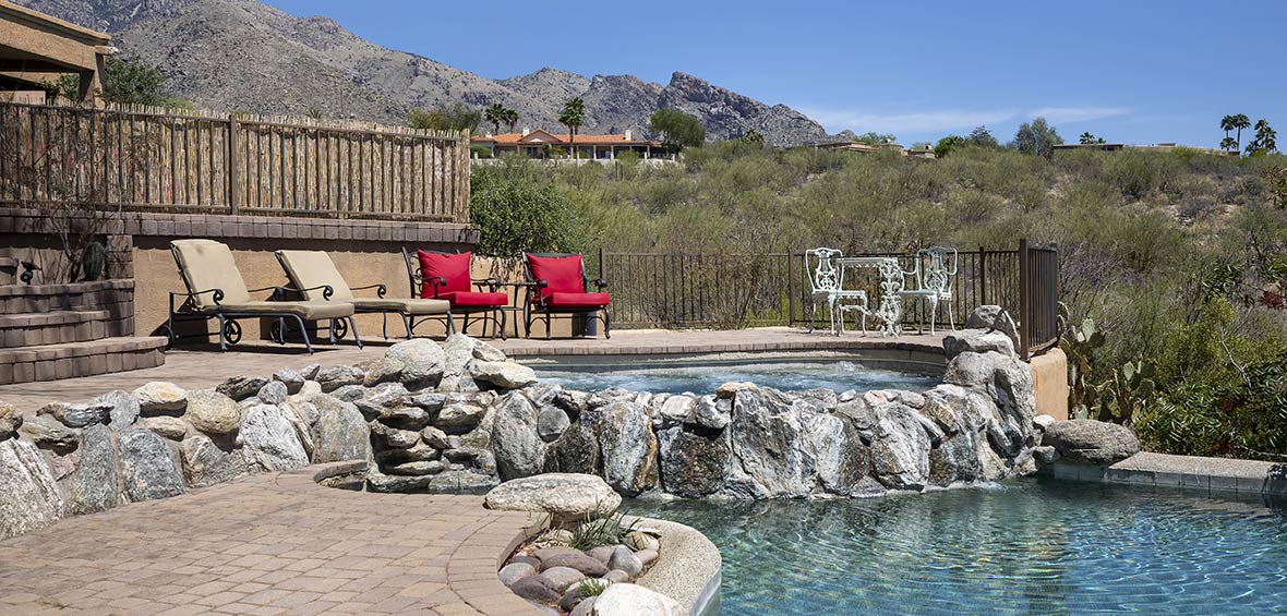 A poolside hot tub is set in an elevated patio with furniture surrounding it. 