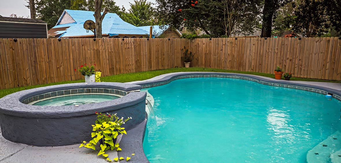 A hot tub feeds water into a neighboring pool and both features are surrounded by a privacy fence. 