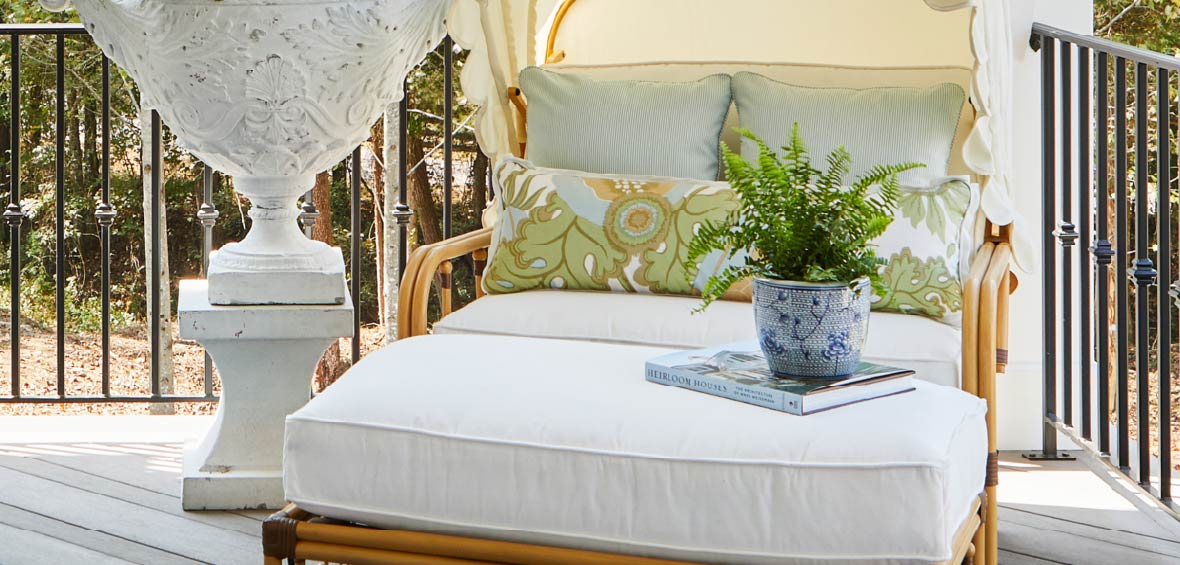 A rattan chair and ottoman with cushions on a deck with a hardback book and potted plant on the ottoman.