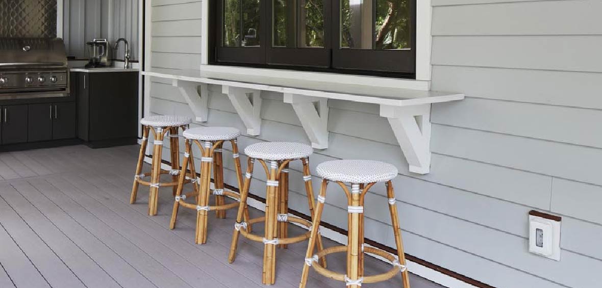 Four barstools are placed under a built-in counter attached to a window with an outdoor kitchen in the background. 