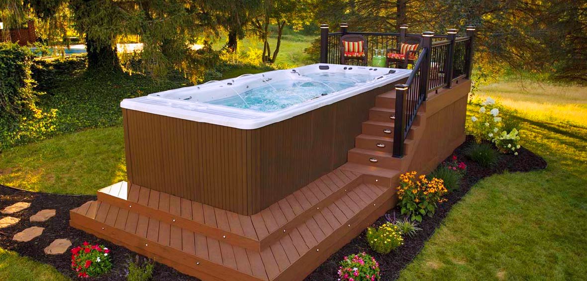 A custom hot tub deck features stairs to an elevated platform to enter the rectangular spa and is surrounded by fresh mulch and landscaping.