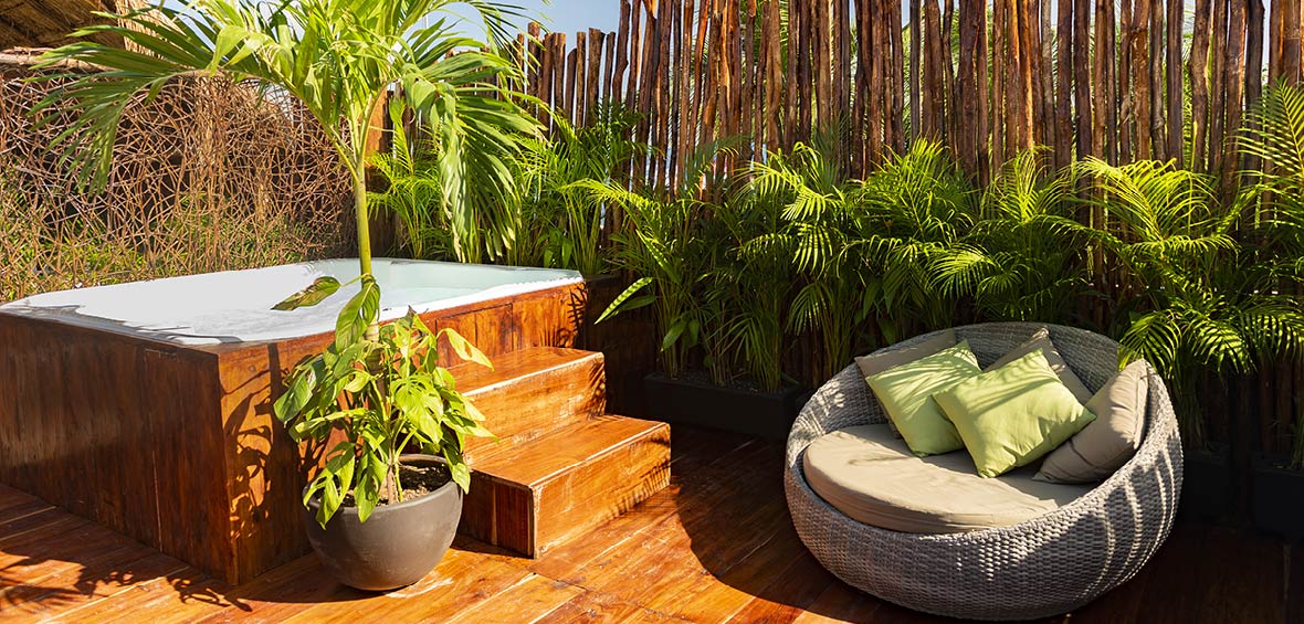 A hot tub is surrounded by organic bamboo fencing with live palms and bamboo offering a natural privacy screen. 