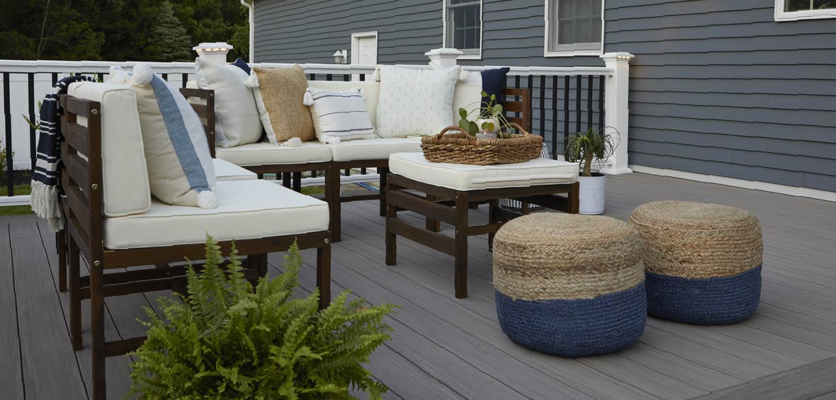 A small deck features minimalist furniture with several plants and pillows for an inviting atmosphere. 