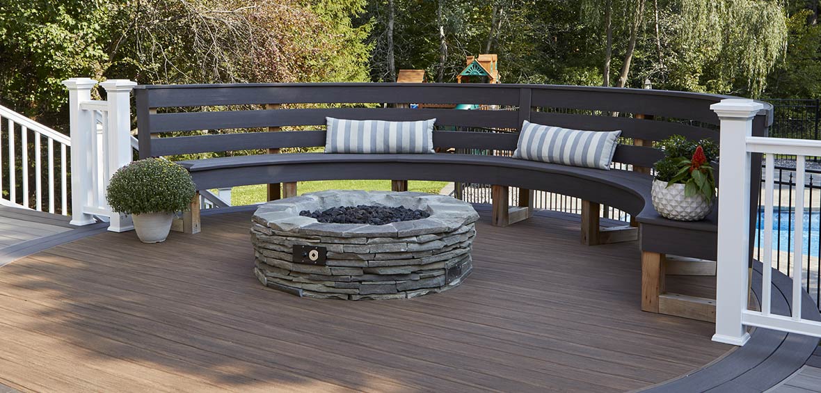 A built-in bench follows the curve of a deck’s perimeter with a fire pit in the center and railing on each side. 
