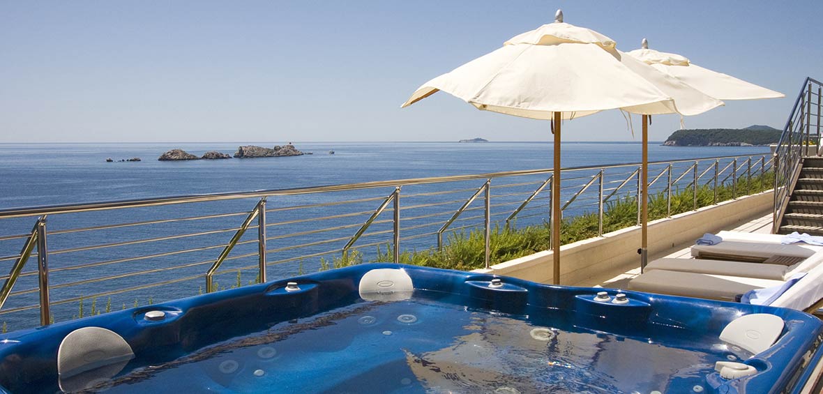 A hot tub overlooks the sea with a few adjacent lounge chairs and umbrellas for shade and privacy.