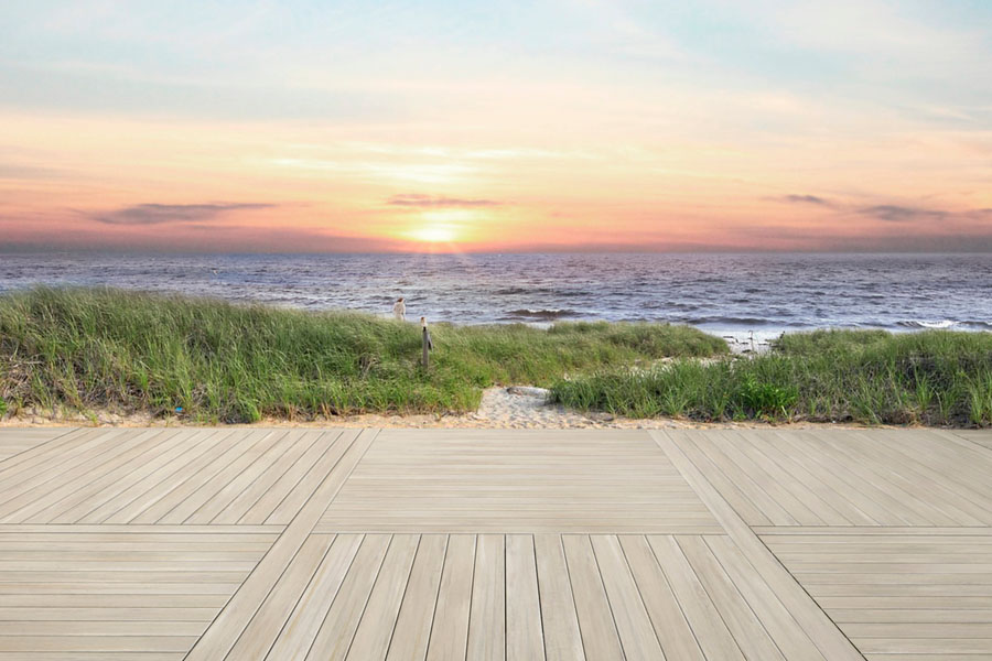 Light tan deck separates the viewer from a grassy beach during sunset