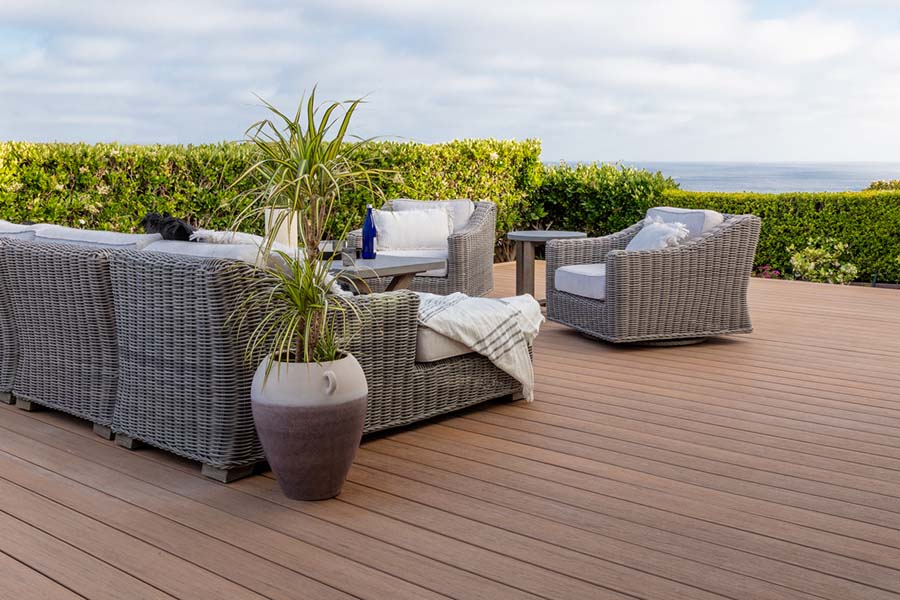 A medium brown deck with grey, wicker furniture and a large potted plant