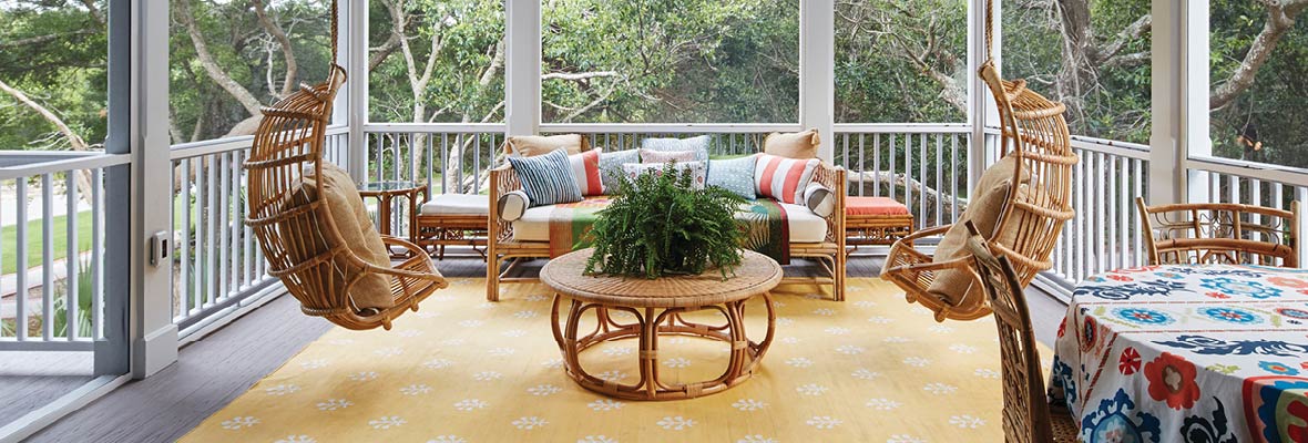 Rattan deck furniture features plush pillows, bold patterns, and potted plants for a cozy aesthetic.